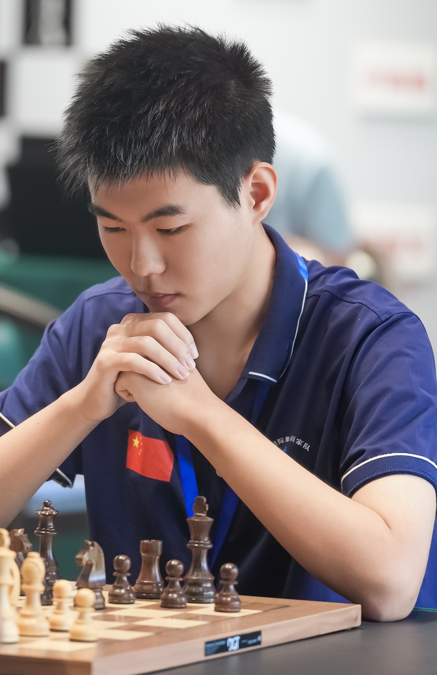 Haowen Xue in deep concentration at the chess board, wearing China national team jersey